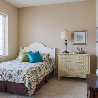 A cozy bedroom with a bed, patterned bedding, and a decorative lamp on a chest of drawers.