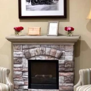 A cozy living room with a stone fireplace, decorated mantel, and striped chairs.