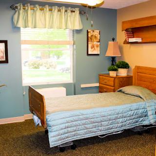 A cozy hospital-style bedroom featuring a single adjustable bed, warm decor, and natural light from a window.
