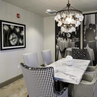 A stylish dining room featuring a marble table, black and white checkered chairs, a decorative chandelier, and monochrome artwork on the walls.