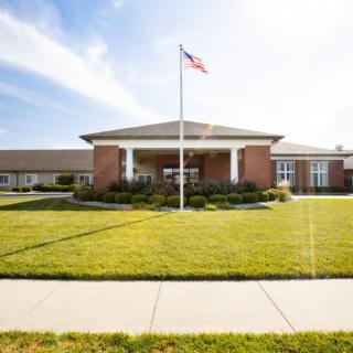 A brick building with an American flag on a flagpole, surrounded by a well-maintained lawn and sidewalk, under a clear blue sky.