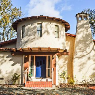 A unique house with a round tower, chimney, and blue door bathed in sunlight.