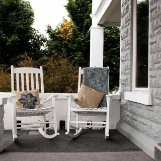 A cozy porch with two white rocking chairs adorned with cushions, set against a stone wall.
