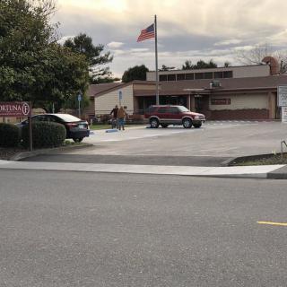 A building with a parking lot, cars, and a flagpole under a cloudy sky.