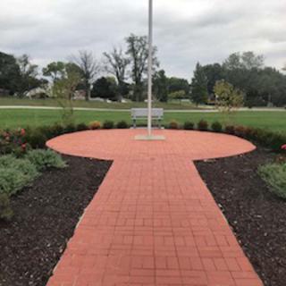 A brick pathway leading to a flagpole, surrounded by landscaped gardens.