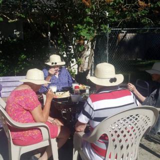 A group of people gathered in a garden, wearing hats and sitting on chairs.