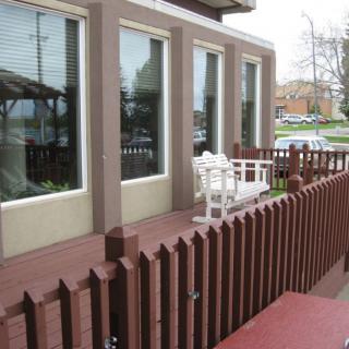 An outdoor patio area with a brown fence and white bench in front of a building with large windows.