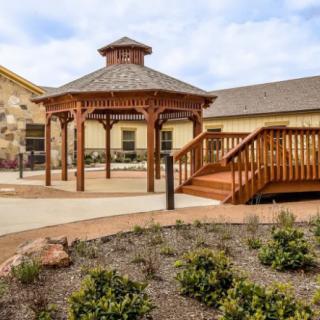 A wooden gazebo in a landscaped garden area next to a building.