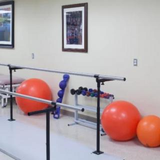 A physical therapy room equipped with parallel bars, therapy balls, and dumbbells.