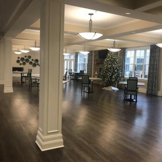 A spacious, elegantly decorated room with wooden floors, chandeliers, and arranged tables and chairs.