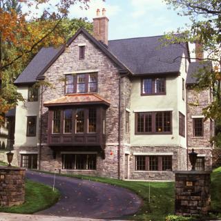 A historic stone house with a paved driveway and surrounding trees.