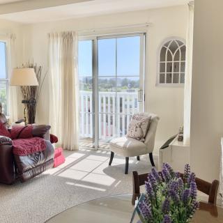A bright and cozy living room with sunlight streaming through large windows, featuring a comfortable armchair and sofa accented with decorative pillows.
