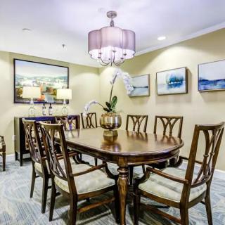 A sophisticated dining room featuring a wooden table surrounded by chairs, adorned with elegant lighting and decorative paintings on the walls.