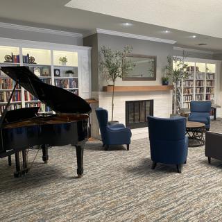 A cozy lounge area featuring a grand piano, bookshelves, and comfortable seating around a fireplace.