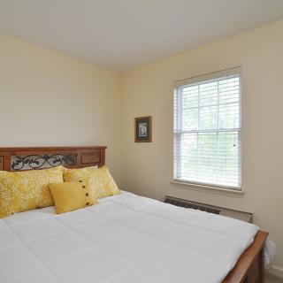 A simple bedroom with a neatly made bed and yellow pillows by the window.