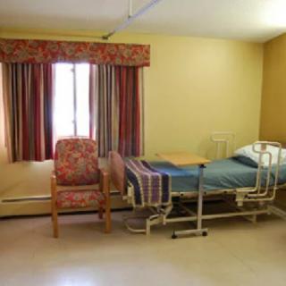 A hospital room with a bed, chair, and window.