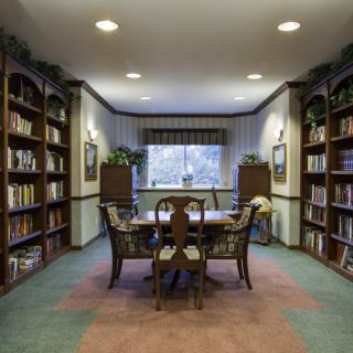 A cozy library reading room with bookshelves lining the walls and a table with chairs in the center.