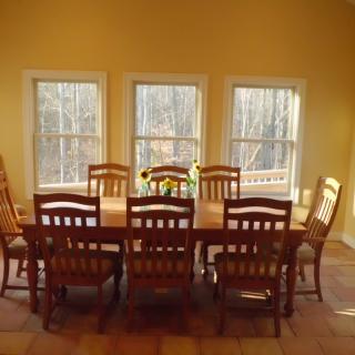 A dining room with a wooden table and chairs, featuring three large windows letting in natural light.