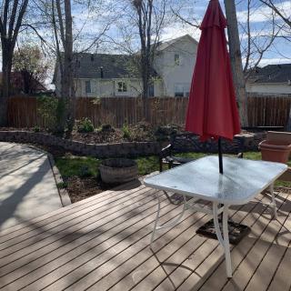A backyard deck with a table and red umbrella, surrounded by trees and garden.