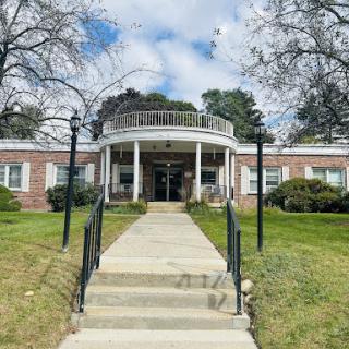 An inviting entrance to a well-maintained building surrounded by greenery and a clear blue sky.