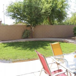 A sunny backyard with a patio, lawn, and chairs.