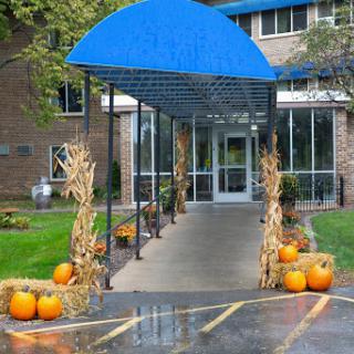 A festive autumn entrance decorated with pumpkins and hay bales under a blue awning.