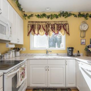 A cozy kitchen with white cabinets, yellow walls, and a window adorned with red and gold curtains.