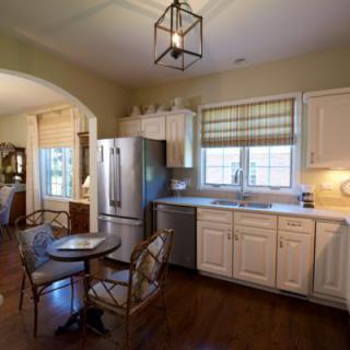 A cozy kitchen interior with white cabinets, stainless steel appliances, and a small dining table by the window.