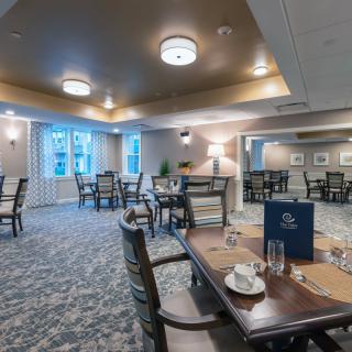 A cozy dining room with neatly arranged tables and chairs, featuring elegant lighting and decor.