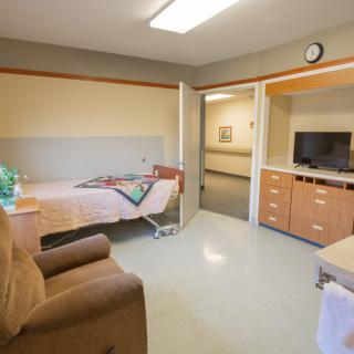 A clean and organized hospital room with a bed, chair, and television.
