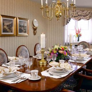 A formal dining room with an elegantly set table, featuring a chandelier and floral centerpiece.