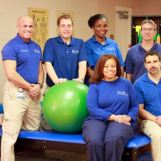 A team of physical therapy professionals posing together with exercise equipment.