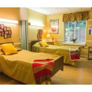 A cozy nursing home room with two neatly made beds and warm lighting.
