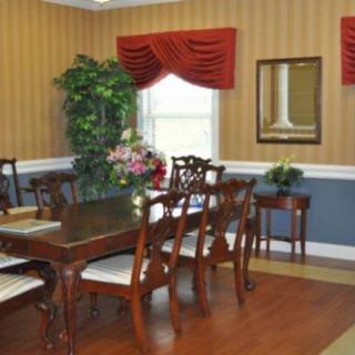 A traditional dining room with a wooden table and chairs, featuring elegant curtains, wall paneling, and decorative plants.