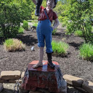 A whimsical statue of a boy striking a playful pose in a garden setting.