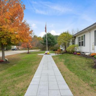 A paved walkway leading to a house with trees showing autumn colors.