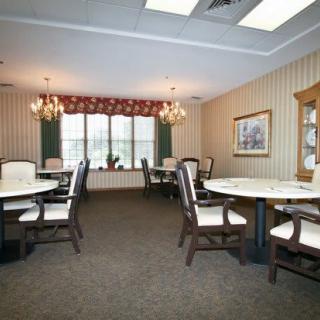 A spacious and elegantly decorated dining room with multiple tables and chairs, featuring chandeliers and a large window.