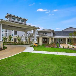 A modern building with a well-maintained green lawn and a covered driveway entrance.