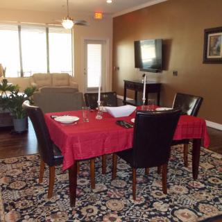 A dining area with a red tablecloth and black chairs, adjacent to a living room featuring a television on the wall.