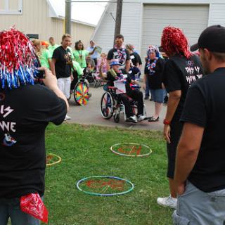 A lively community event featuring participants engaged in various activities, including a person in a wheelchair surrounded by supporters.