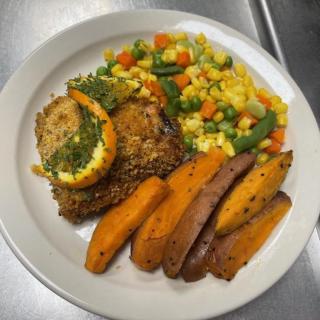 A plate with stuffed chicken, seasoned potato wedges, and mixed vegetables.