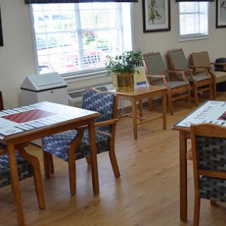 A cozy waiting area featuring wooden tables and chairs, illuminated by natural light from a nearby window.