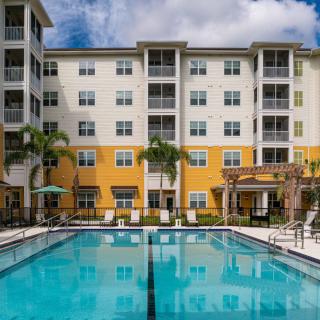 Modern apartment complex with a swimming pool and palm trees.
