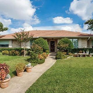 A suburban house with a well-maintained lawn and garden under a bright blue sky.