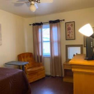 A cozy bedroom with a desk, chair, and window with curtains.