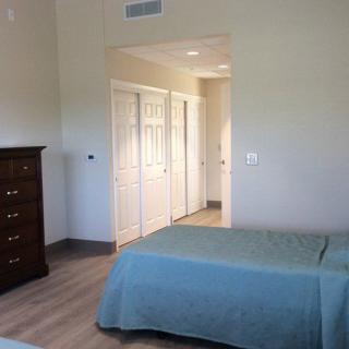A bedroom featuring a bed with a blue bedspread, a wooden dresser, and a view of the hallway leading to closets.