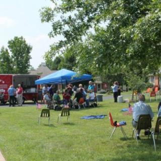 A group of people gathered under a tent in a park on a sunny day.