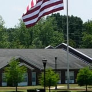 A large American flag flies in front of a building surrounded by trees.