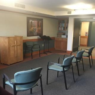 A small chapel with a few chairs and a podium featuring a cross.