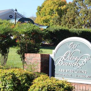 Entrance sign for a senior living community surrounded by greenery.